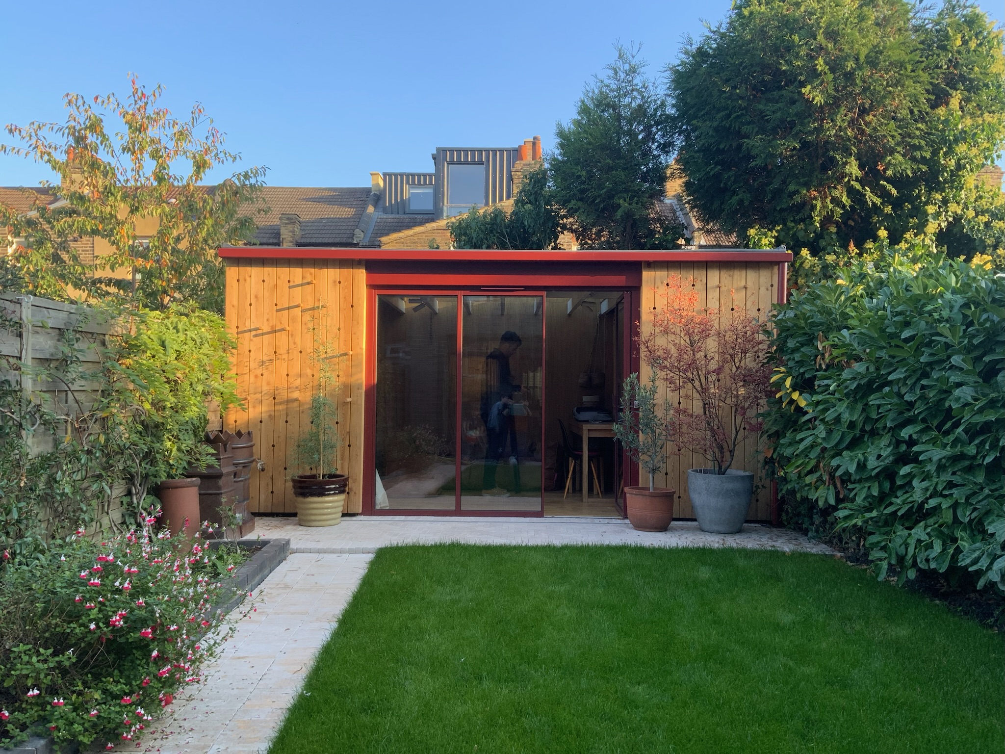 The materials palette is natural and tactile: oak timber flooring, European larch cladding, and a limestone patio provide warmth and texture. Powder-coated aluminium features and door frames in a soft oxide red take their cue from the Acer tree in the garden. Underfloor heating ensures comfort year-round.</p>
<p>The design was carefully considered to meet the needs of a young family while retaining a calm, open feel and an attractive aesthetic when viewed from the house.