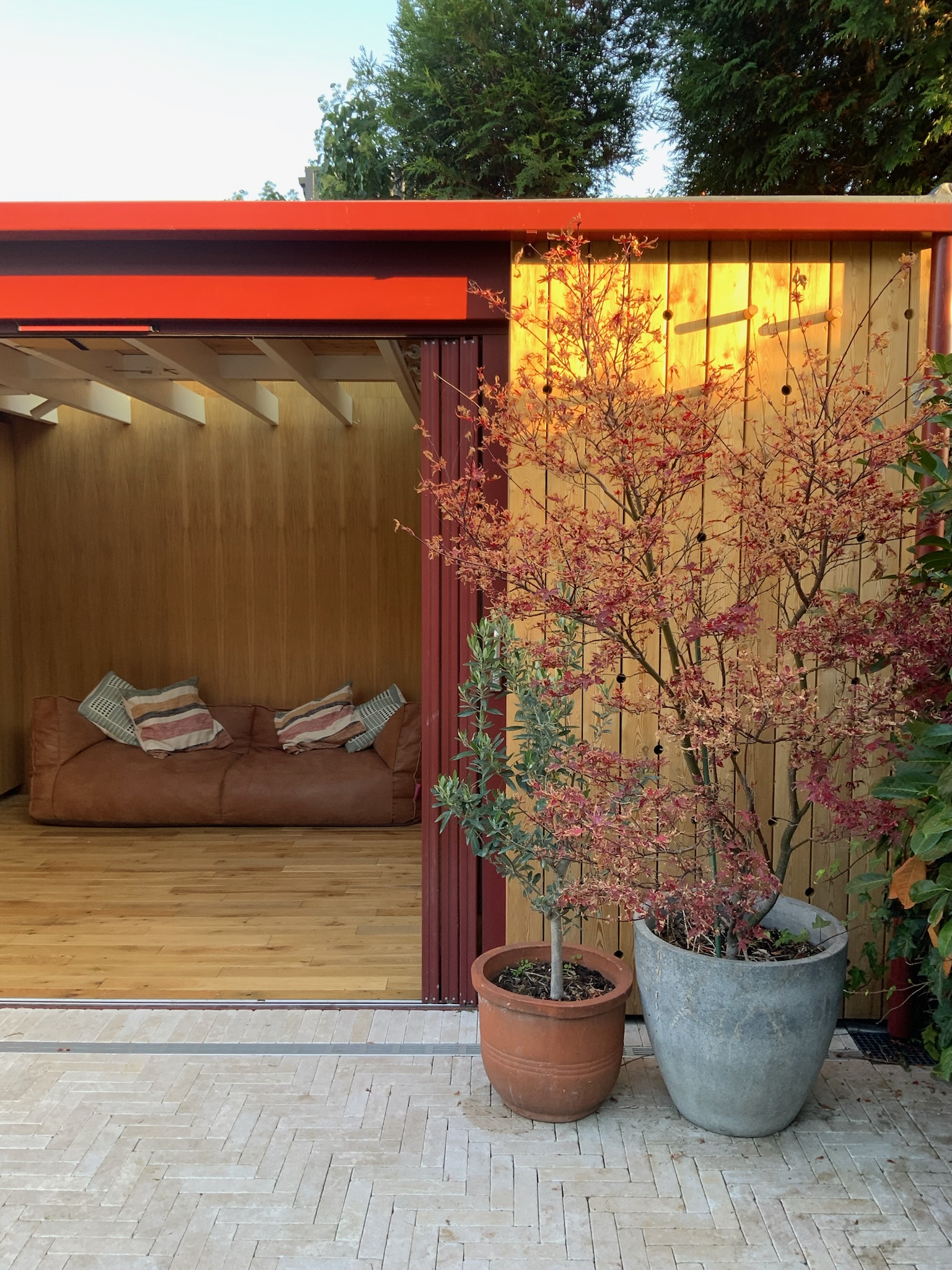 The materials palette is natural and tactile: oak timber flooring, European larch cladding, and a limestone patio provide warmth and texture. Powder-coated aluminium features and door frames in a soft oxide red take their cue from the Acer tree in the garden. Underfloor heating ensures comfort year-round. The design was carefully considered to meet the needs of a young family while retaining a calm, open feel and an attractive aesthetic when viewed from the house.